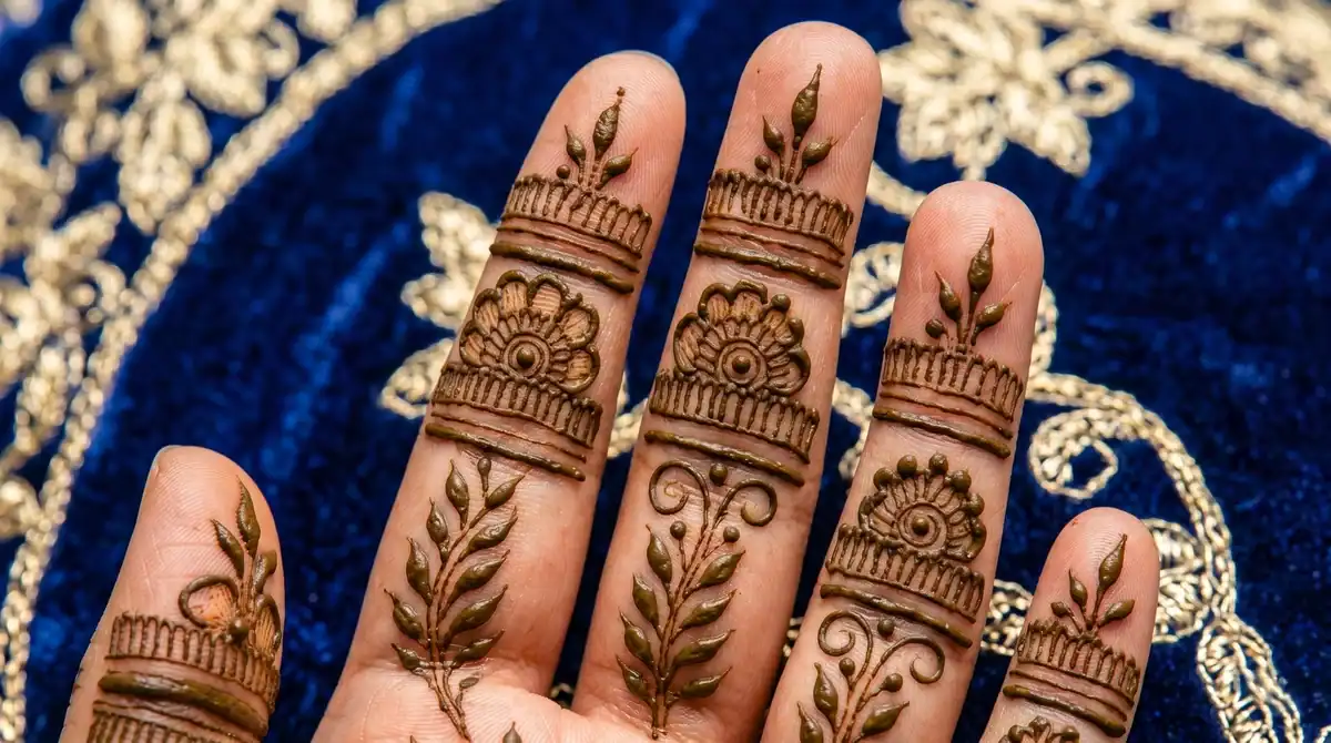 Stylish Arabic finger mehndi design showing bold floral crowns and stacked ring bands on the back of five fingers against blue velvet